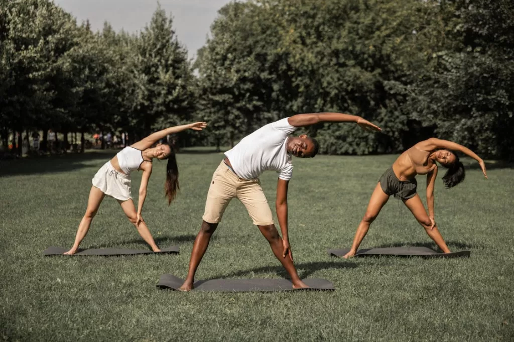 um homem e duas mulheres fazendo alongamentos ao ar livre mostrando estilos de yoga para iniciantes