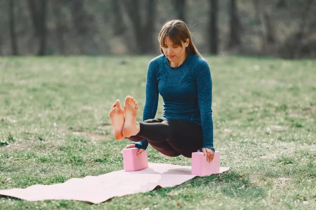 Uma mulher ao ar livre fazendo yoga com blocos rosas em um gramado verde e bonito.