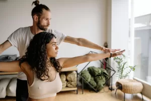 Um homem dando um curso de formação em yoga em um estúdio de yoga, ajudando a esticar os braços e fazer movimentos.