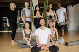 um estúdio de yoga com um instrutor de yoga reconhecido pelo mec dando curso com várias pessoas olhando para a câmera num estúdio de yoga.