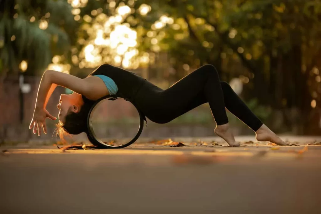 Uma mulher ao ar livre praticando yoga com uma roda de yoga que fica embaixo das costas dela.